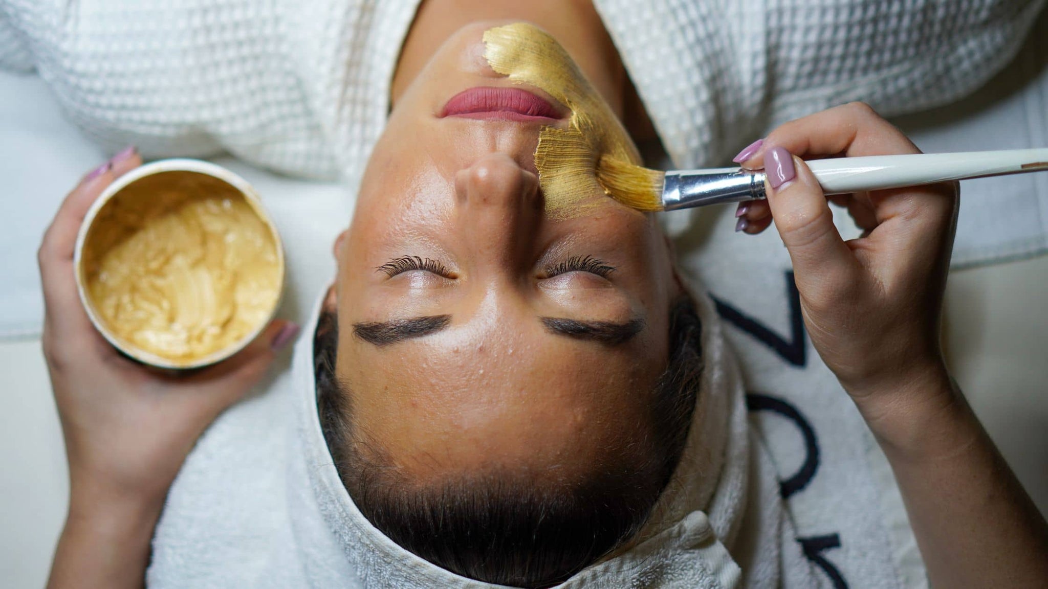 Spa facial treatment applying a golden banana-based mask with brush