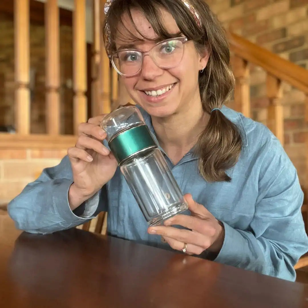 Girl holding a Green Tea Infuser Bottle by Us and The Earth - Enjoy your favorite tea on-the-go with our eco-friendly glass bottle.