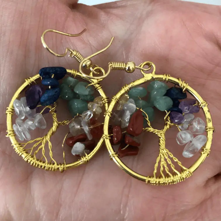 A hand gently holds a pair of 'Tree of Life' earrings, displaying their intricate beauty.
