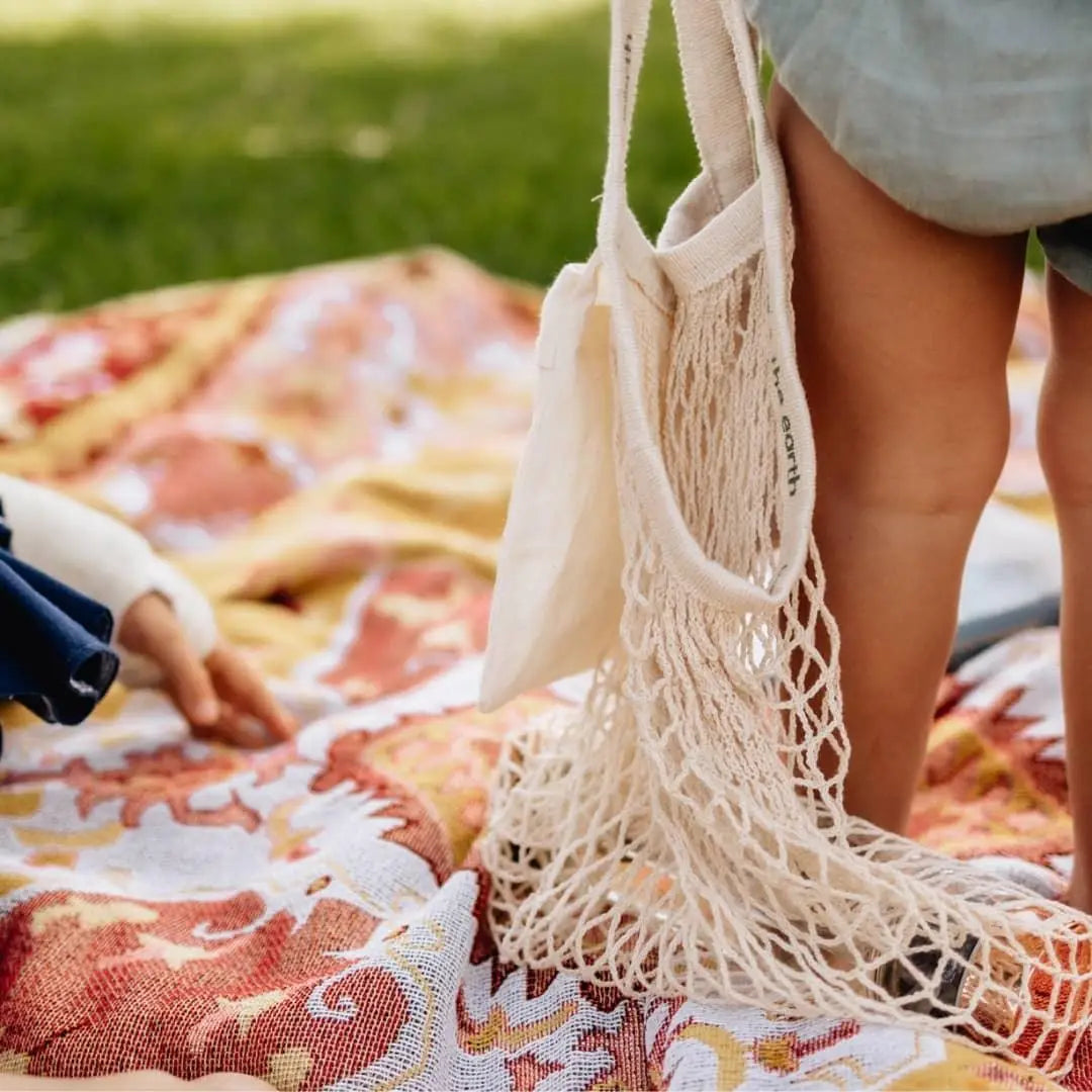 A child's legs holding a Reusable Shopping Net Bag, a symbol of eco-friendly habits from a young age.