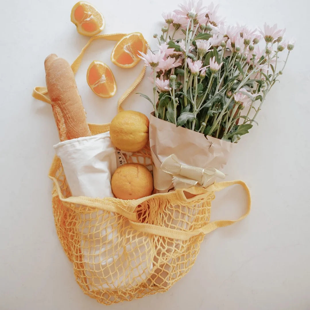 A Reusable Shopping Net Bag adorned with bread, oranges, and flowers, symbolizing sustainable and vibrant shopping choices.